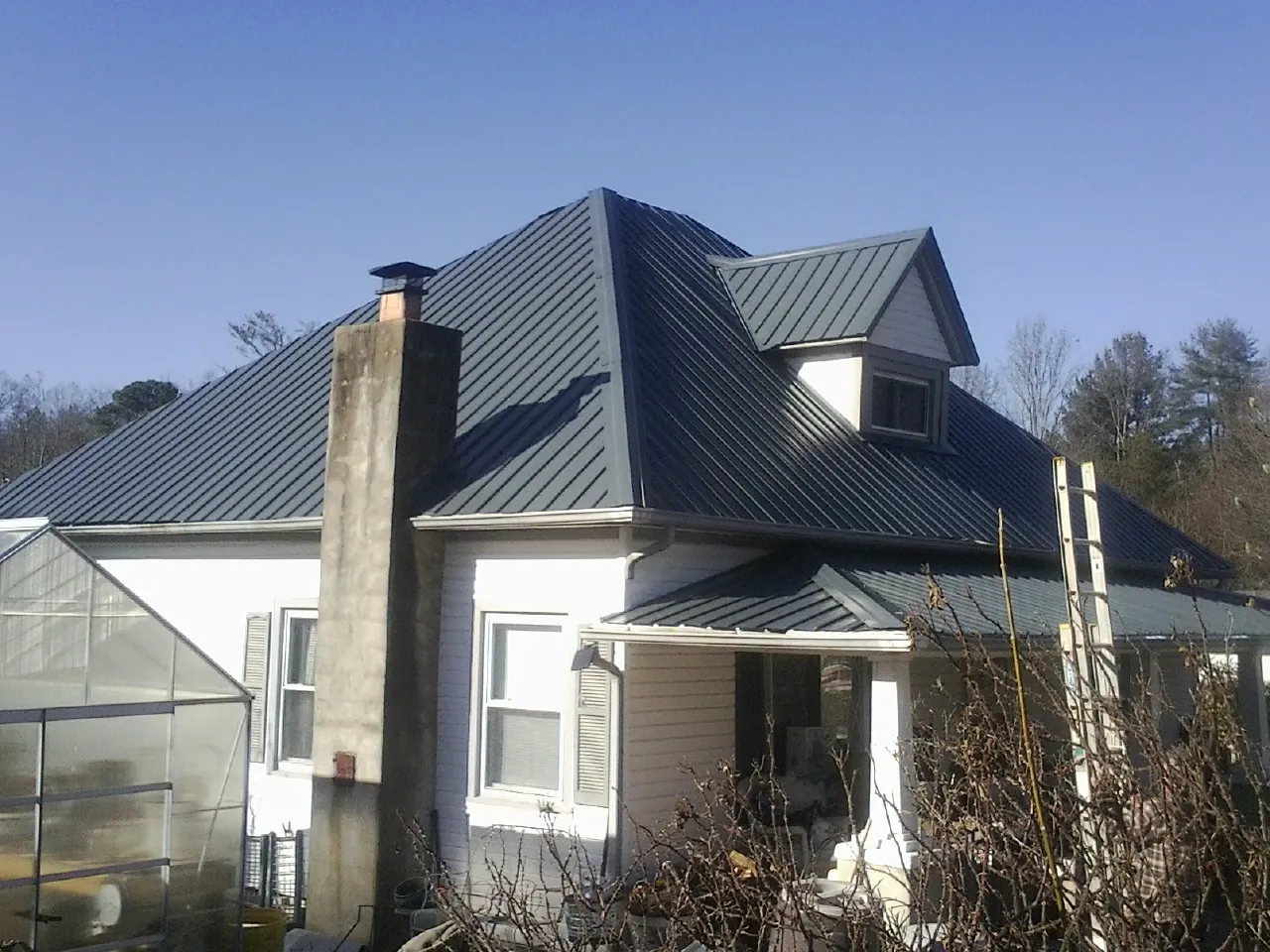 Dark blue standing seam metal roof on a white farmhouse with dormer — Slate & Tile Roof Repair by Roofing Brothers in North Scituate