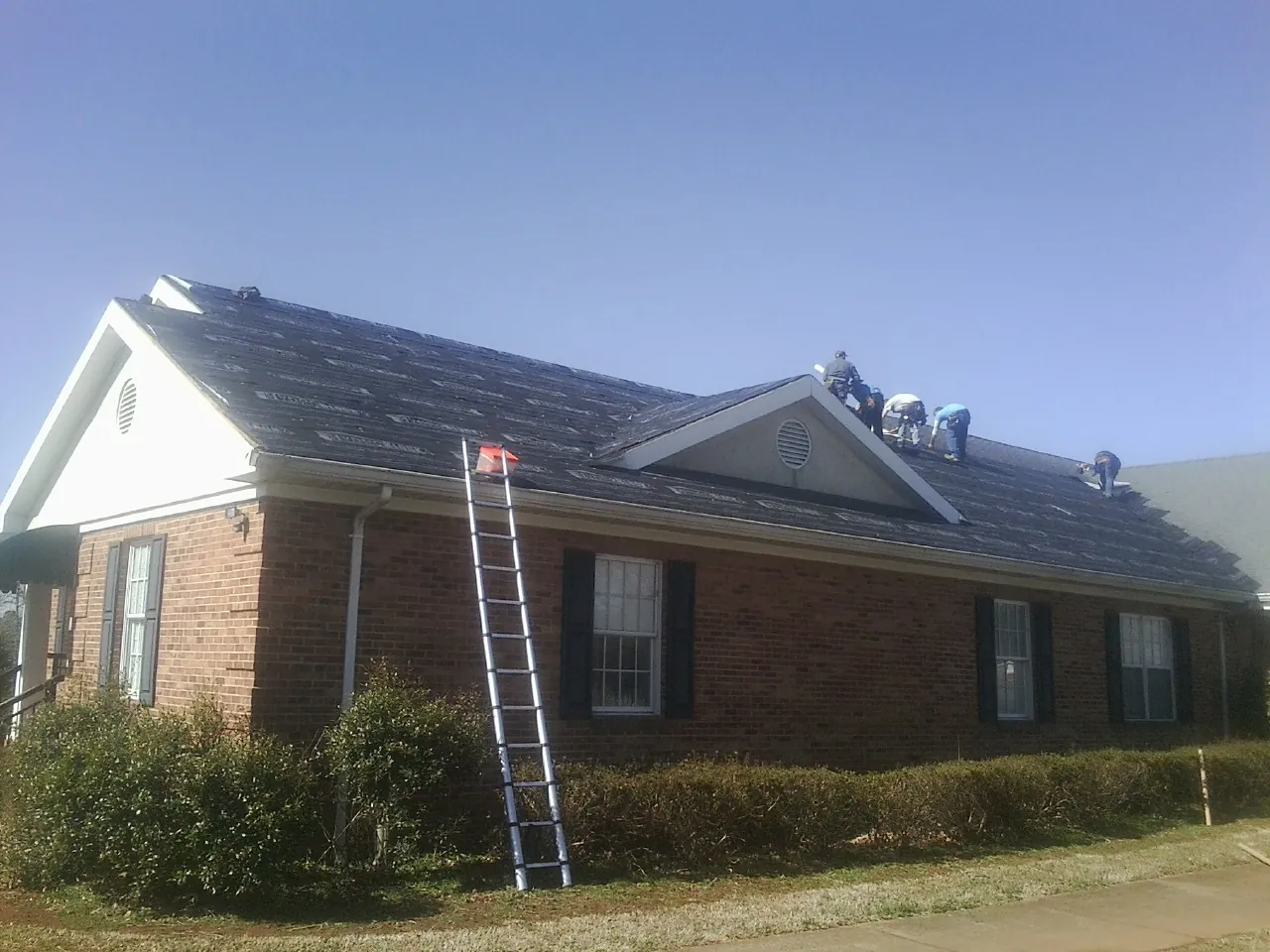 Crew tearing shingles off a brick ranch roof with a ladder set — Metal Roof Repair work by our crew in North Scituate