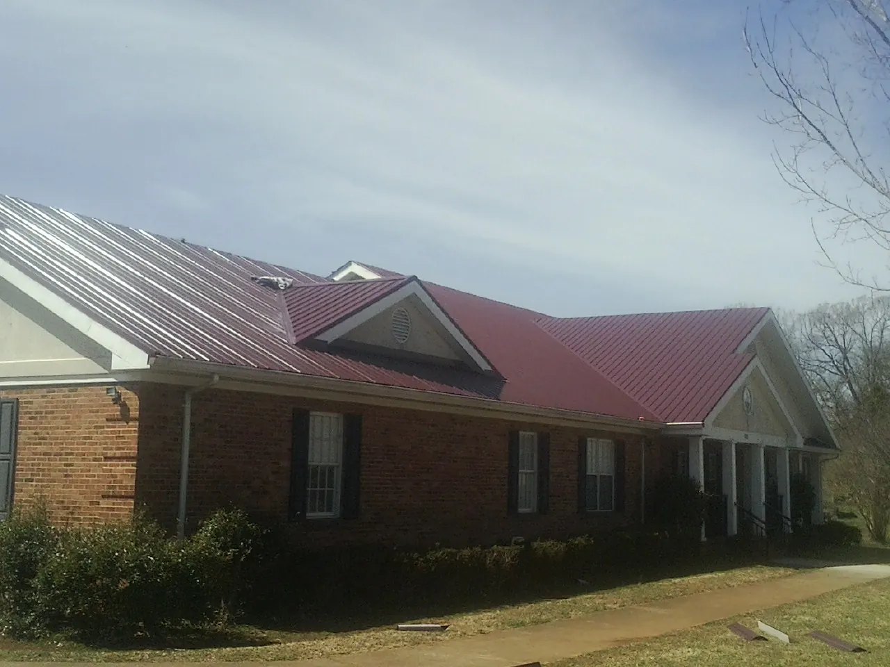 Red metal roof with gabled entries on a long brick building, from a Hail Damage Roof Repair job in North Scituate