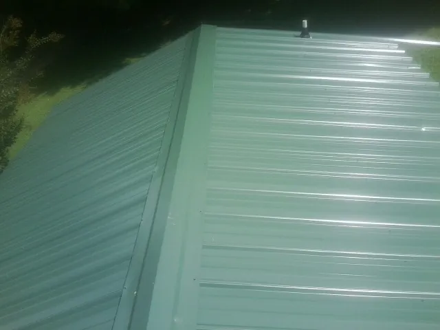 New green metal panels meeting at the ridge of a roof — Flat Roof Repair work by our crew in North Scituate
