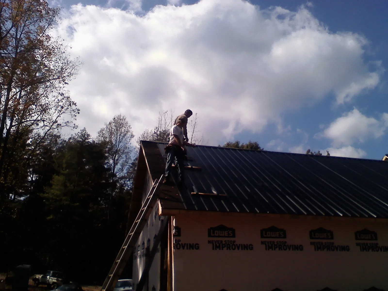 Roofer fastening dark metal panels high against a cloudy sky, from a Roof Inspection job in North Scituate