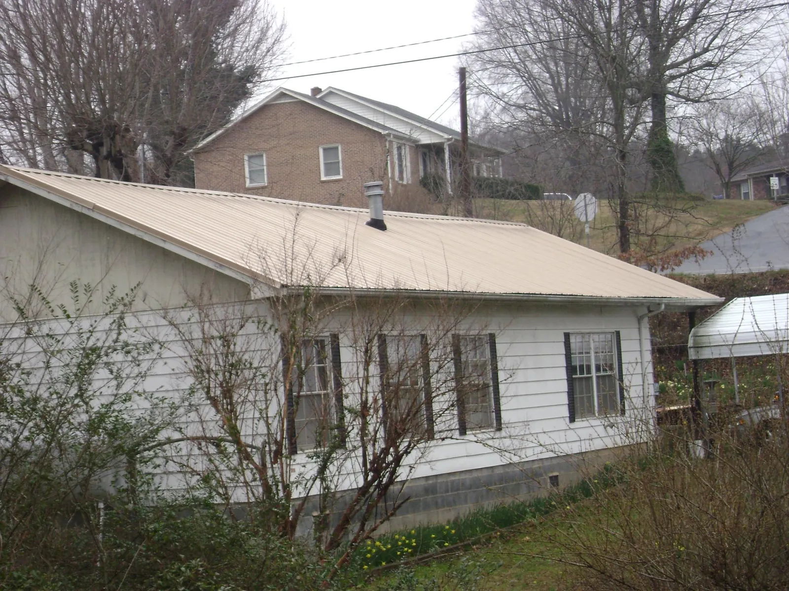 Tan metal roof on a white sided house set into a hillside — Commercial Roofing by Roofing Brothers in North Scituate